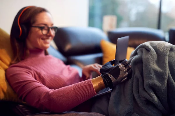 Woman Prosthetic Arm Wearing Wireless Headphones Working Laptop Sofa Home — стоковое фото