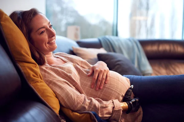 Gravid Kvinna Med Protes Arm Avslappnande Ligga Soffan Hemma Holding — Stockfoto