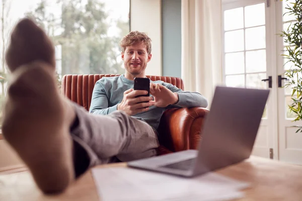 Man Relaxing Armchair Feet Home Using Laptop Mobile Phone — Fotografia de Stock