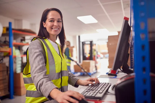 Portrait Of Female Manager In Busy Modern Warehouse Working On Computer Terminal