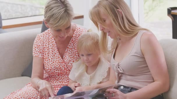 Granddaughter Sitting Sofa Grandmother Mother Looking Photo Album Together Shot — Stockvideo