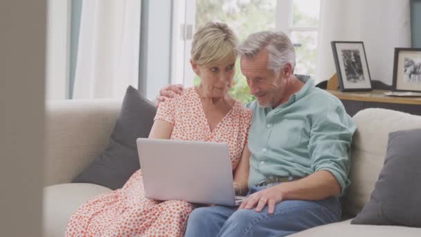 Smiling Senior Retired Couple Sitting Sofa Home Booking Holiday Shopping — Vídeo de Stock