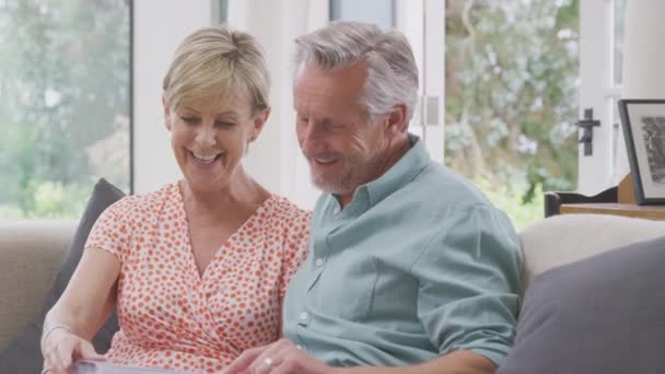 Smiling Senior Couple Sitting Sofa Home Looking Photo Album Together — Stockvideo