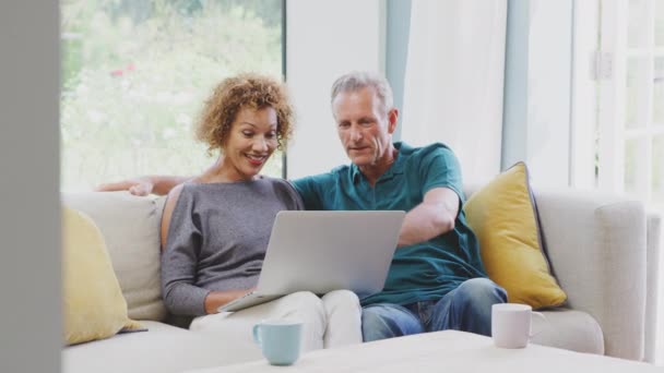 Smiling Senior Retired Couple Sitting Sofa Home Booking Holiday Shopping — Wideo stockowe