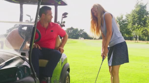 乘坐高尔夫球车的男子在女子练习高尔夫球杆时给她提建议 慢动作射击 — 图库视频影像