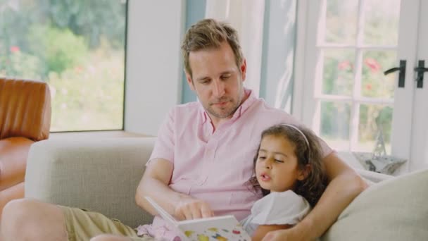 父亲和女儿一起坐在沙发上看书 动作缓慢 — 图库视频影像