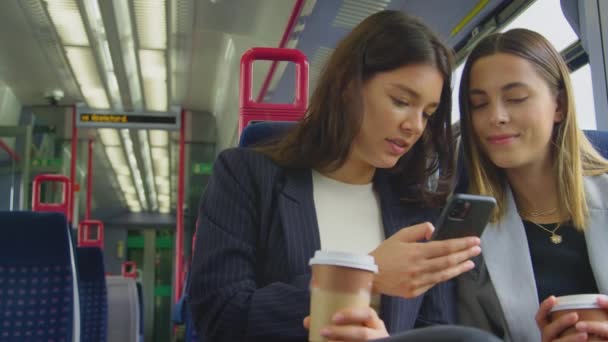 Two Businesswomen Takeaway Coffees Commuting Work Train Looking Mobile Phone — Stok video