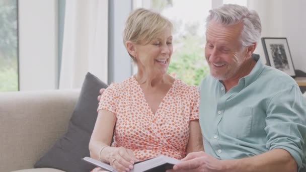 Smiling Senior Couple Sitting Sofa Home Looking Photo Album Together — Vídeos de Stock