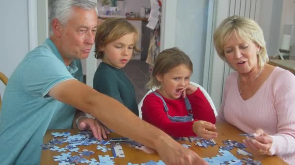 Grandchildren Grandparents Sitting Table Home Doing Jigsaw Puzzle Together Shot — Stok video