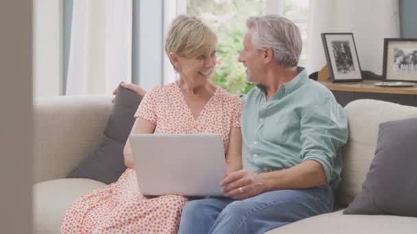Smiling Senior Retired Couple Sitting Sofa Home Booking Holiday Shopping — Vídeo de Stock