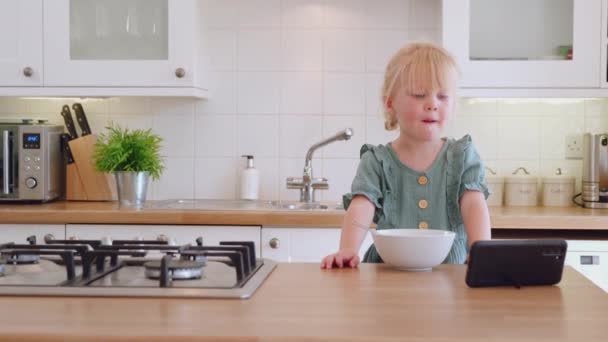 Nagranie Pięknej Dziewczynki Jedzącej Śniadanie Oglądającej Kreskówki Smartfonem — Wideo stockowe