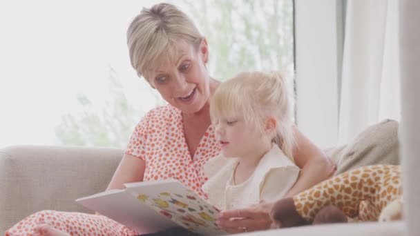 Granddaughter Sitting Sofa Grandmother Reading Story Book Together Shot Slow — Vídeo de Stock