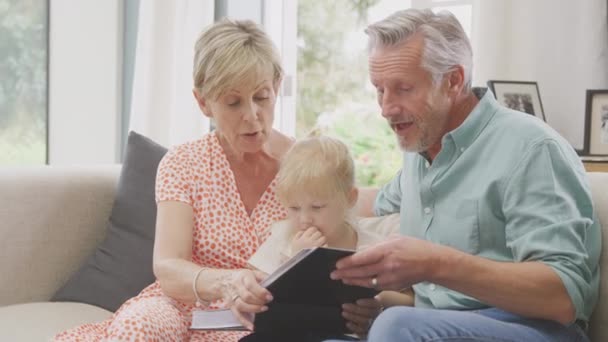 Grandparents Sitting Sofa Home Granddaughter Looking Photo Album Together Shot — Vídeo de Stock