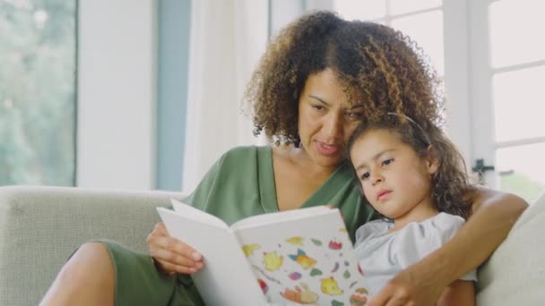 母亲和女儿一起坐在家里的沙发上看书 动作缓慢 — 图库视频影像