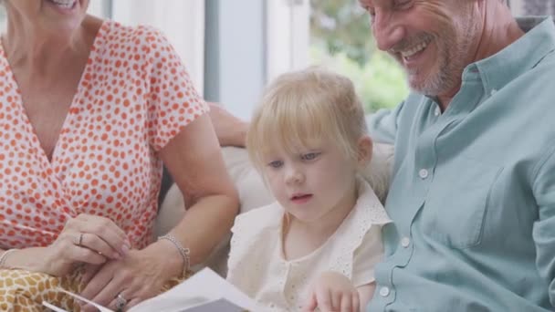 Close Granddaughter Sitting Sofa Grandparents Reading Story Book Together Shot — Wideo stockowe