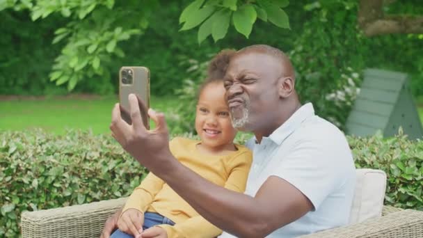 Grandfather Pulling Faces Granddaughter Taking Selfie Mobile Phone Garden Home — Stockvideo