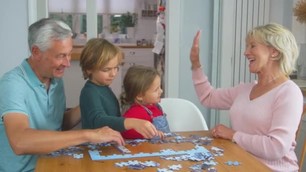 Grandchildren Grandparents Sitting Table Home Doing Jigsaw Puzzle Together Shot — Vídeos de Stock