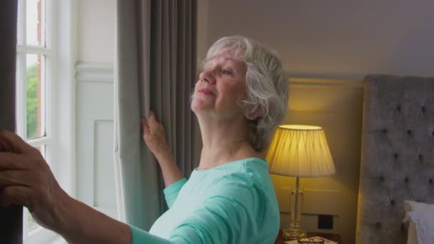 Χαμογελαστή Ηλικιωμένη Γυναίκα Στο Σπίτι Φορώντας Πιτζάμες Τραβώντας Κουρτίνες Στην — Αρχείο Βίντεο