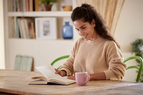 Kvinna Avslappnande Hemma Sitter Vid Bordet Läsbok Med Varm Dryck — Stockfoto