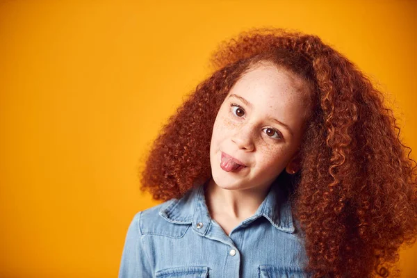 Studio Portrait Of Smiling Young Girl Pulling Funny Face Shot Against Yellow Background