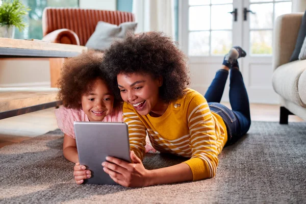 母と娘は一緒に自宅でデジタルタブレットで床のストリーミング映画に横たわって楽しみを持っています — ストック写真