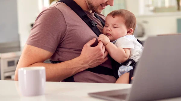 自宅から働くトランスジェンダーの父ノートパソコンでスリングで赤ちゃんの息子の世話をする — ストック写真