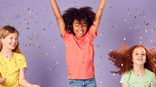 紫色の背景に延長腕を持つ空気中でキラキラジャンプしている子供たちのスタジオショット — ストック写真