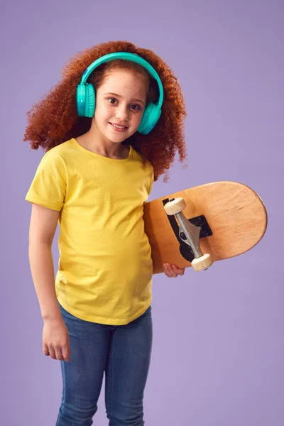 Studio Shot Young Girl Noszenie Słuchawek Trzymając Deskorolkę Fioletowym Tle — Zdjęcie stockowe