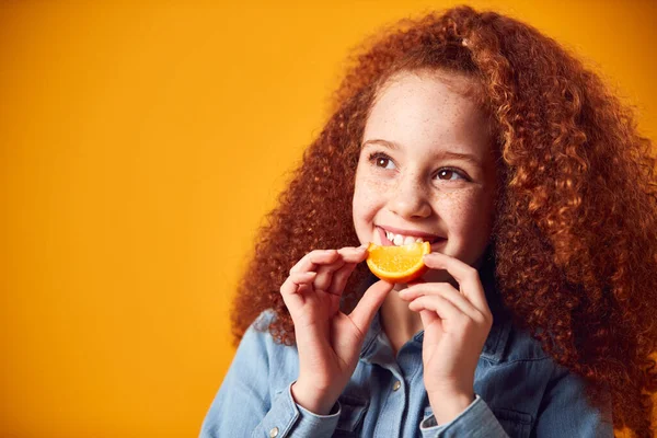 浅谈在黄色背景下张大嘴笑的女孩持橙的画室肖像 — 图库照片