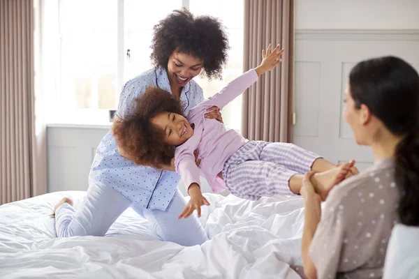 有两个妈妈的家庭穿着睡衣和女儿在床上玩耍 — 图库照片