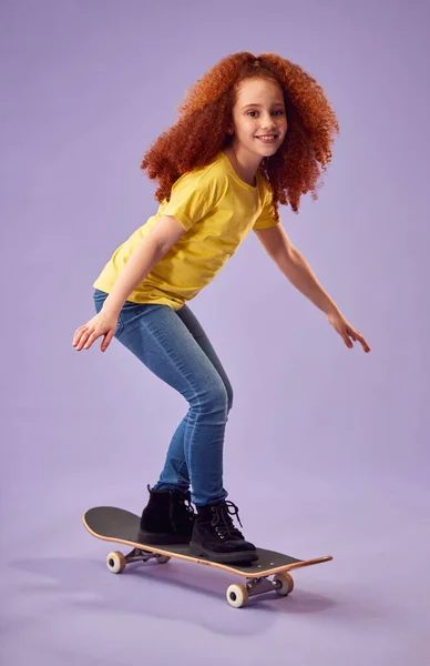 Studio Shot Van Jong Meisje Paardrijden Skateboard Tegen Paarse Achtergrond — Stockfoto