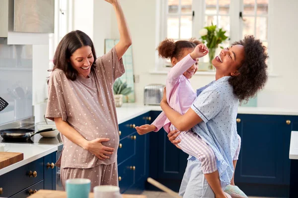 两个妈妈的怀孕家庭穿着睡衣和女儿在厨房里跳舞 — 图库照片