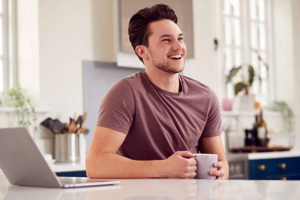 Transgender Man Working From Home Looking At Laptop On Kitchen Counter