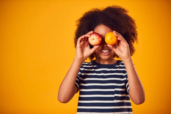 黄色の背景に目の前でアップルとオレンジを保持する少年のスタジオ肖像画 — ストック写真