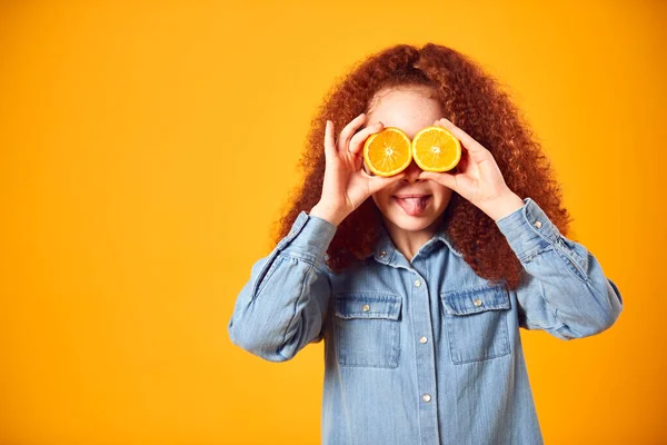 黄色の背景に目の前に2つのオレンジの半分を保持している女の子のスタジオ肖像画 — ストック写真