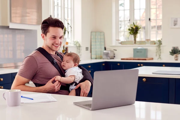 自宅から働くトランスジェンダーの父ノートパソコンでスリングで赤ちゃんの息子の世話をする — ストック写真