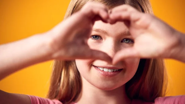 Gülümseyen Kızın Stüdyo Portresi Sarı Arkaplan Karşısında Elleriyle Kalp Şekli — Stok fotoğraf
