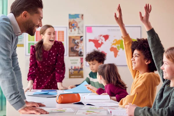 Group Of Multi-Cultural Students With Teachers In Classroom Putting Hand Up To Answer Question