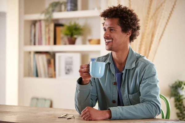 Hombre Sonriente Relajándose Casa Sentado Mesa Con Bebida Caliente —  Fotos de Stock