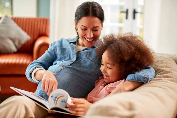 怀孕的母亲和女儿一起在家里看书放松对沙发的依赖 — 图库照片