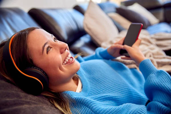 自宅で携帯電話から音楽を聴くワイヤレスヘッドフォンを身に着けている10代の女の子 — ストック写真