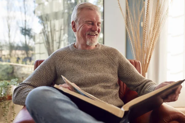 Glimlachende Senior Man Thuis Genietend Kijkend Door Fotoalbum Samen — Stockfoto