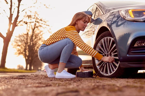 田舎道で電動ポンプで車のタイヤをインフレ女性 — ストック写真