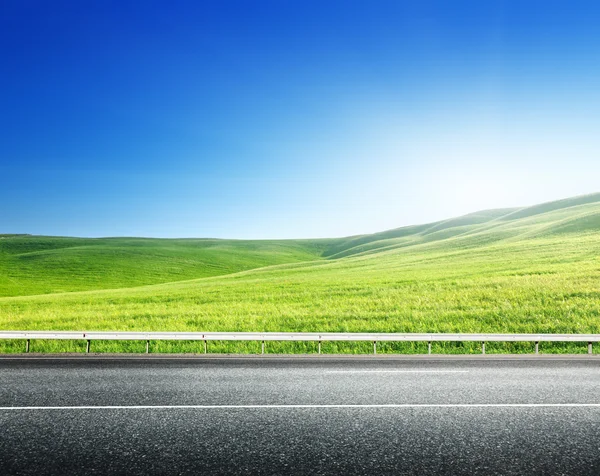 Asphalt road and perfect green field — Stock Photo, Image