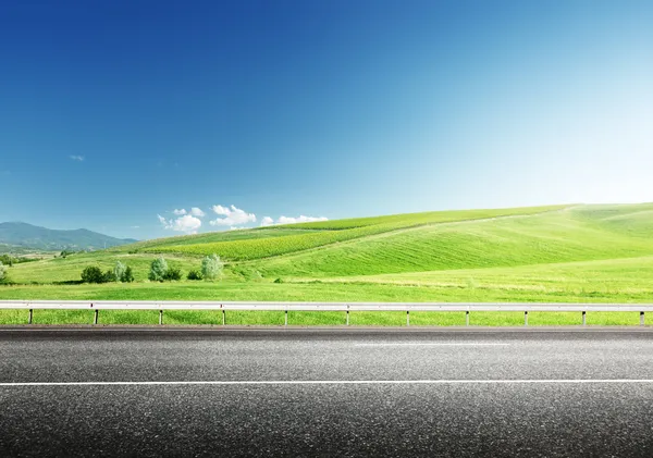 Asphalt road and perfect green field — Stock Photo, Image