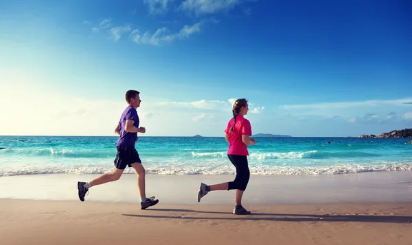 Hombre y mujeres corriendo en la playa tropical al atardecer —  Fotos de Stock