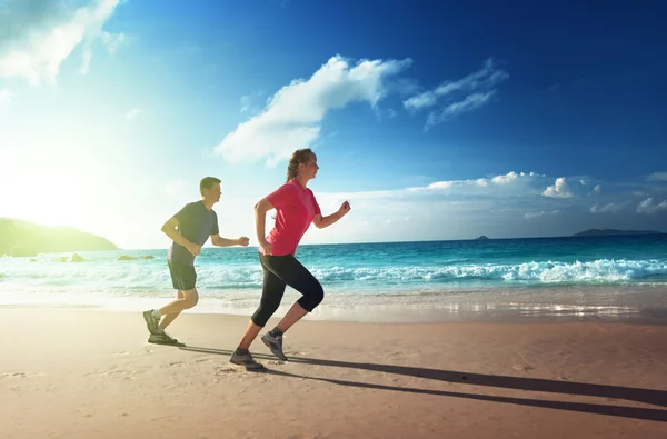 Uomo e donna che corrono sulla spiaggia tropicale al tramonto — Foto Stock