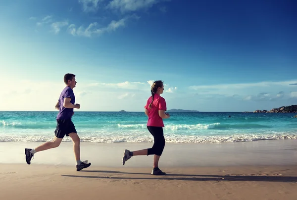 男子和妇女在日落时在热带海滩上奔跑 — 图库照片