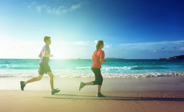 男子和妇女在日落时在热带海滩上奔跑 — 图库照片