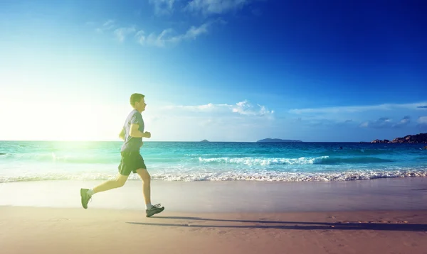 Muž běží na tropické pláži při západu slunce — Stock fotografie